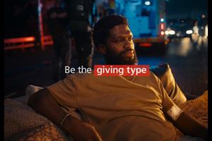 A man lying on a sofa with an ambulance behind him and text saying 'Be the giving type'