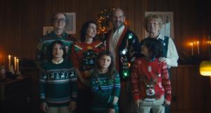 A family stands together, all wearing Christmas sweaters