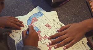 Hands are seen coloring in states on a map of the United States