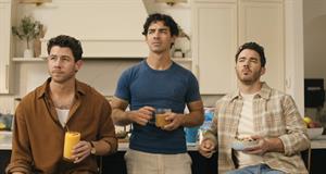 The Jonas Brothers in a kitchen holding various breakfast food and drink items