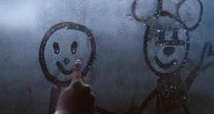 A child's hand draws a smiley face and Mickey Mouse on window condensation