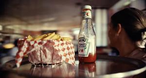 A waitress holds a tray with a basket of French fries and a bottle of Heinz ketchup