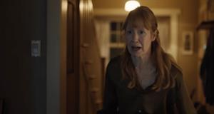 A woman stands in her home looking shocked by something she sees off screen
