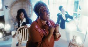 A woman is singing, two people are seen blurred in the background
