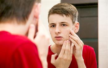 A young man looks at his complexion in the mirror with a concerned expression.