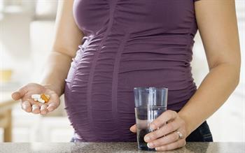 Close up of pregnant lady's bump and one hand containing multiple tablets and the other with a glass of water 