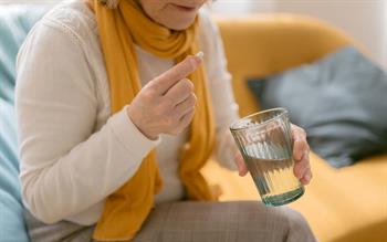 A woman wearing a yellow scarf takes a pill with a glass of water.