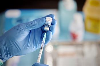 A blue-gloved hand withdraws a dose of COVID-19 vaccine from a vial into a syringe.