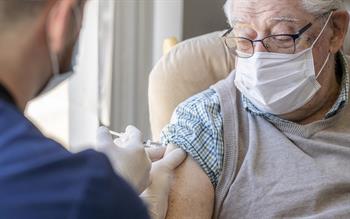 An elderly man looks down at his arm as a male healthcare professional administers his COVID-19 vaccine.