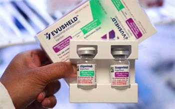 A hand holding a pack of Evusheld vials.