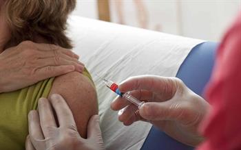 A woman holds up her sleeve so a healthcare professional can administer her flu vaccination.