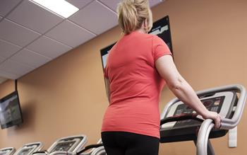 Close up image of a woman in a red t-shirt on a treadmill, shown from behind