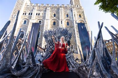 A woman in a red dress sits on the Iron Throne