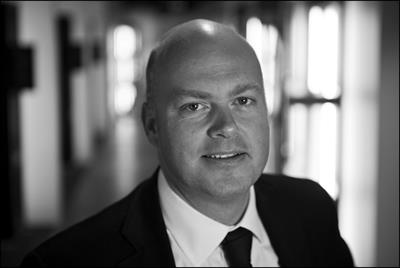 A black and white photo of News UK's Chris Longcroft wearing a dark business suit