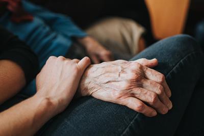 A young person's hand rests comfortingly on the wrist of an elderly person