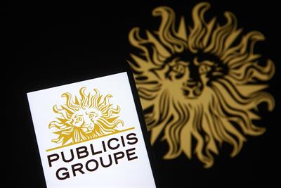A photo of the Publicis Groupe lion's head logo out of focus in the background, with a mobile device bearing the branding in the foreground