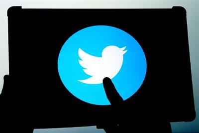 A silhouette of a tablet device and a finger tapping an enlarged Twitter logo lit in bright blue and white