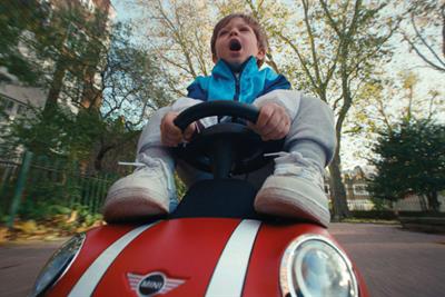 A boy driving a toy Mini along a leafy street