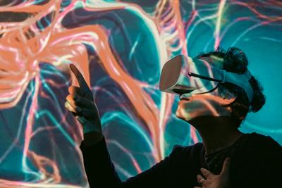 Person wearing a virtual reality headset pointing at projection of abstract shapes and colors