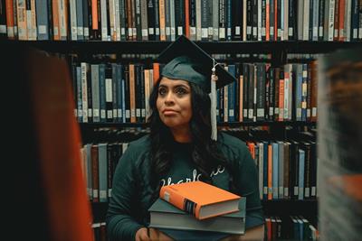 Woman in college graduation gown in library stacks