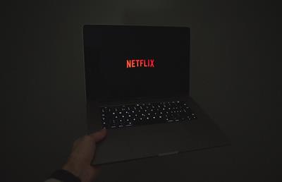 Hand holding laptop with Netflix logo on screen