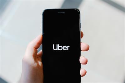 Hand holding smart phone displaying Uber logo
