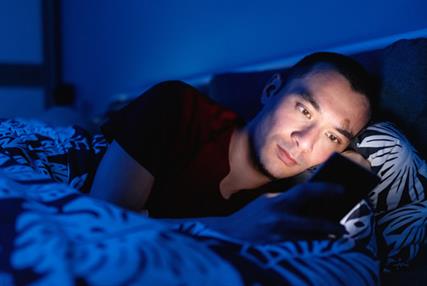 A man lying in bed at night looking at his phone