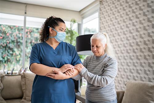 Care home worker with a mask on helping a resident walk around the care home