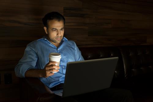 Man working on laptop in dark with coffee