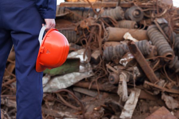 Worker holding helmet, scrap pile