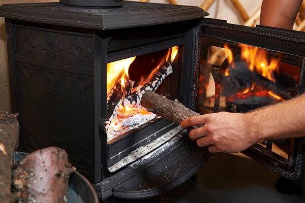 Person putting log into wood burner. Photograph: Ian Allenden/123RF