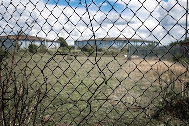 Brownfield land and abandoned gas holders seen through wire fence