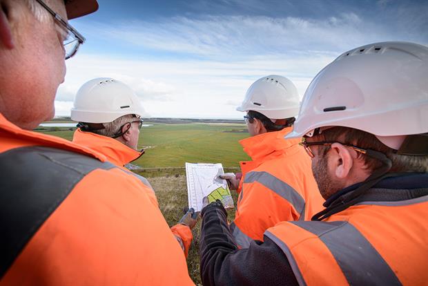 Men in high-vis suits and hard hats in a field looking at a plans