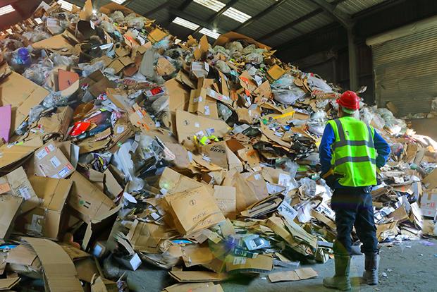 Waste depot workers looking up at a pile of cardboard packaging