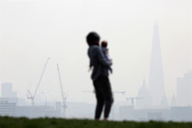 Woman holding a baby looking a smog-filled view of London