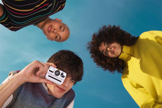 Three people look at the camera. One is holding a Polaroid camera to their eye. (Image: Polaroid)