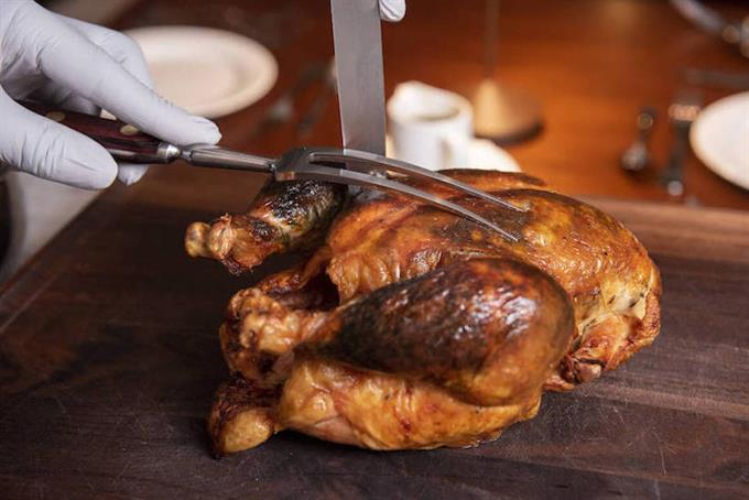 Hands using cutlery to carve chicken on cutting board