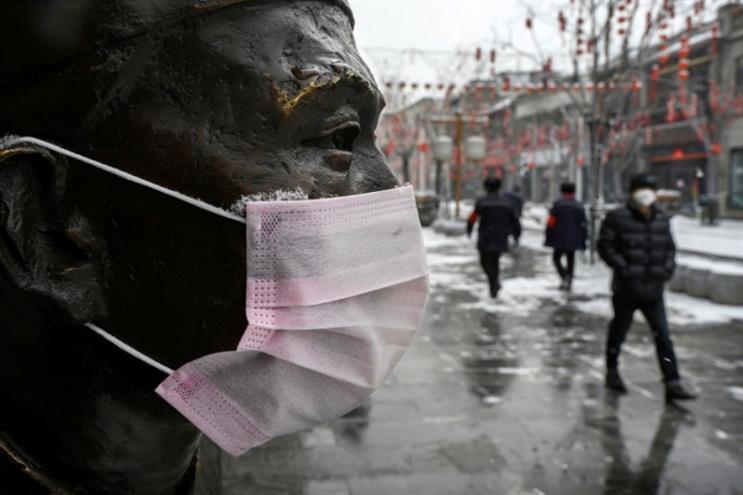 A protective mask is seen on a statue as people walk by in a shuttered street in Beijing (Getty Images)