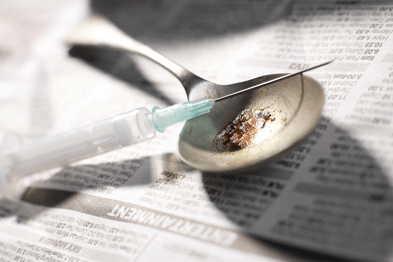 Heroin abuse. Hypodermic needle and syringe with a pile of heroin on a spoon. (SPL)