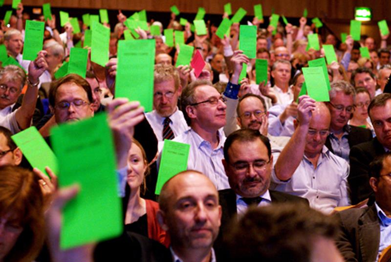 GPs at an LMC conference waving green voting cards in the air