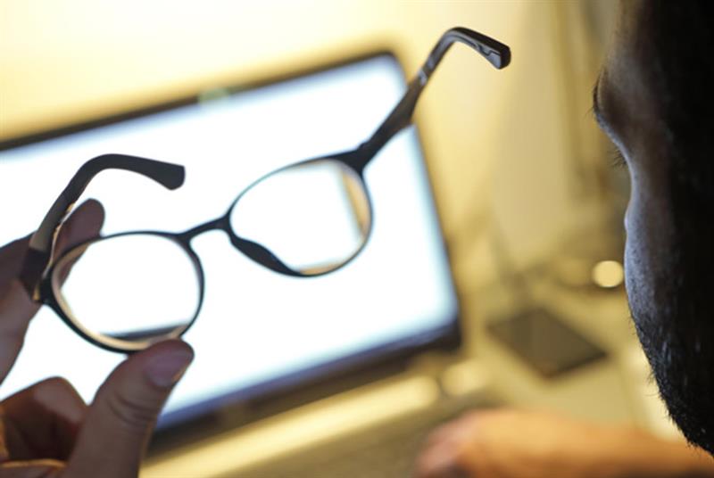 Person holding glasses while looking at a computer