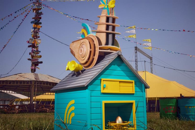 A wooden rooster sits on top of a colourful mini-house. A golden egg lies inside the house