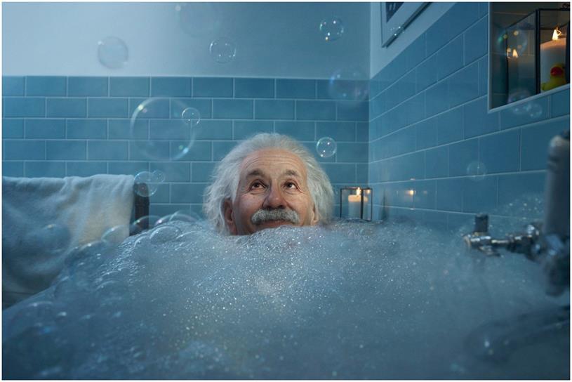 Albert Einstein smiles in a tub filled with bubble bath 