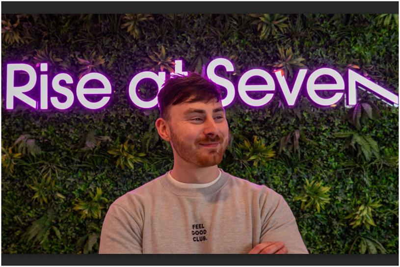 Head shot of Nick Handley standing in front of Rise at Seven neon sign