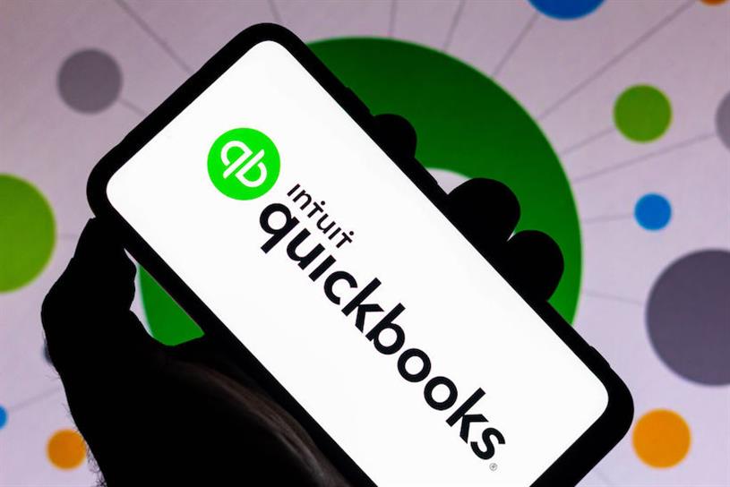 Man holding phone displaying the Intuit Quickbooks app logo.