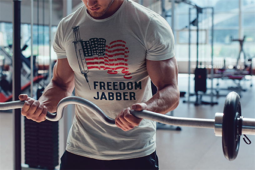 Muscular man in gym lifting weights and wearing a pro-vaccine shirt that reads "freedom jabber"
