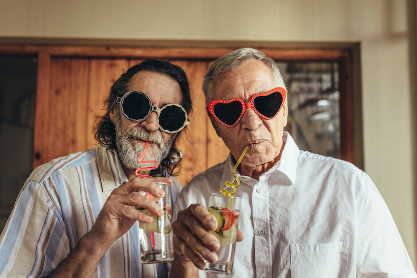 Two men wearing jazzy sunglasses stare into the camera while sipping cocktails