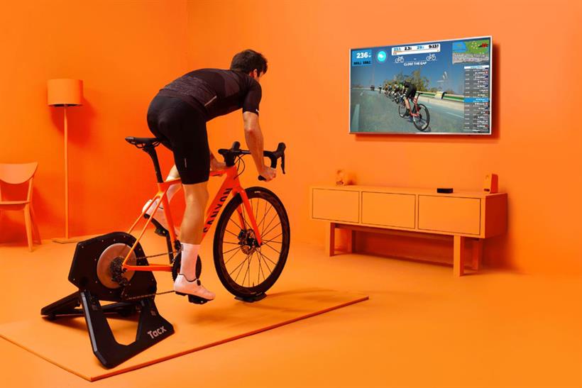 A man on a static bicycle in a luridly orange room, playing online game Zwift, which allows people to compete with other users while they train.