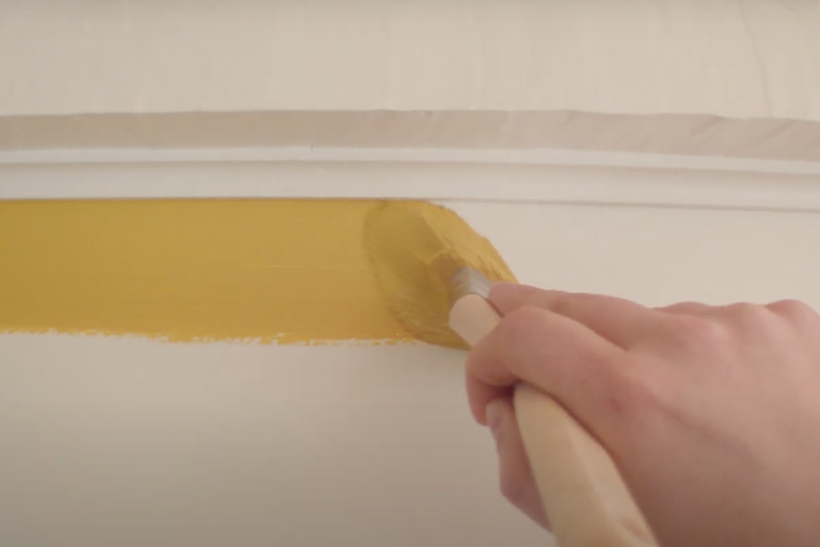 Hand holding paintbrush painting yellow stripe on a white wall