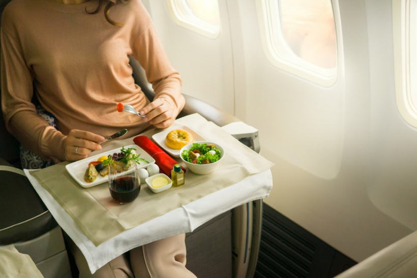 Woman eating from tray of food while sitting in an airplane seat